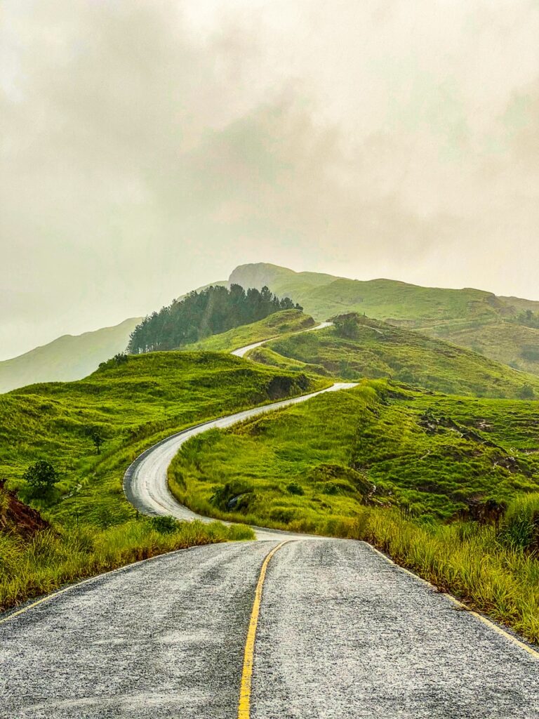 gray concrete road between green grass covered hills